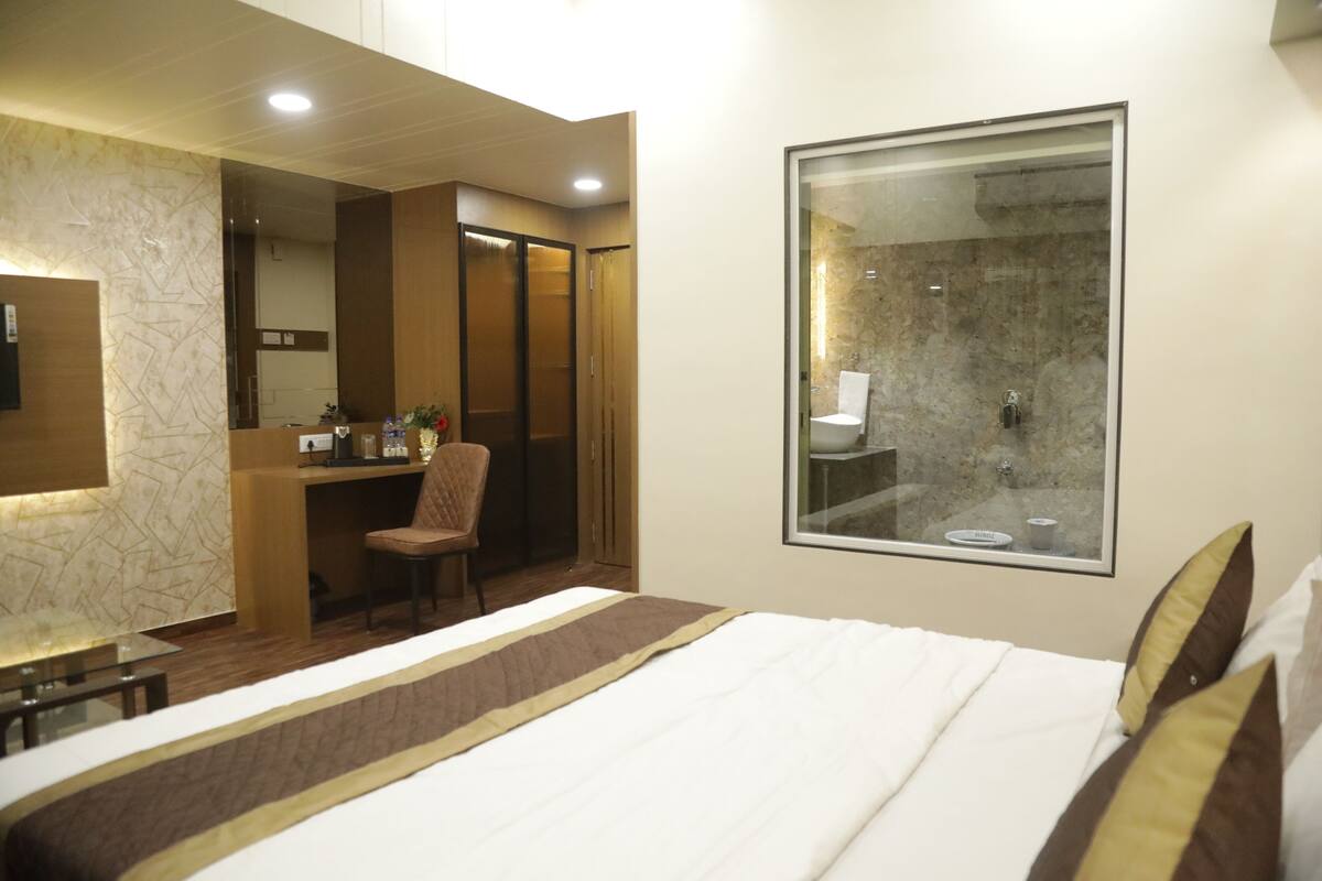 A hotel room with a bed, a desk, a chair, a shower area, and a large window.
