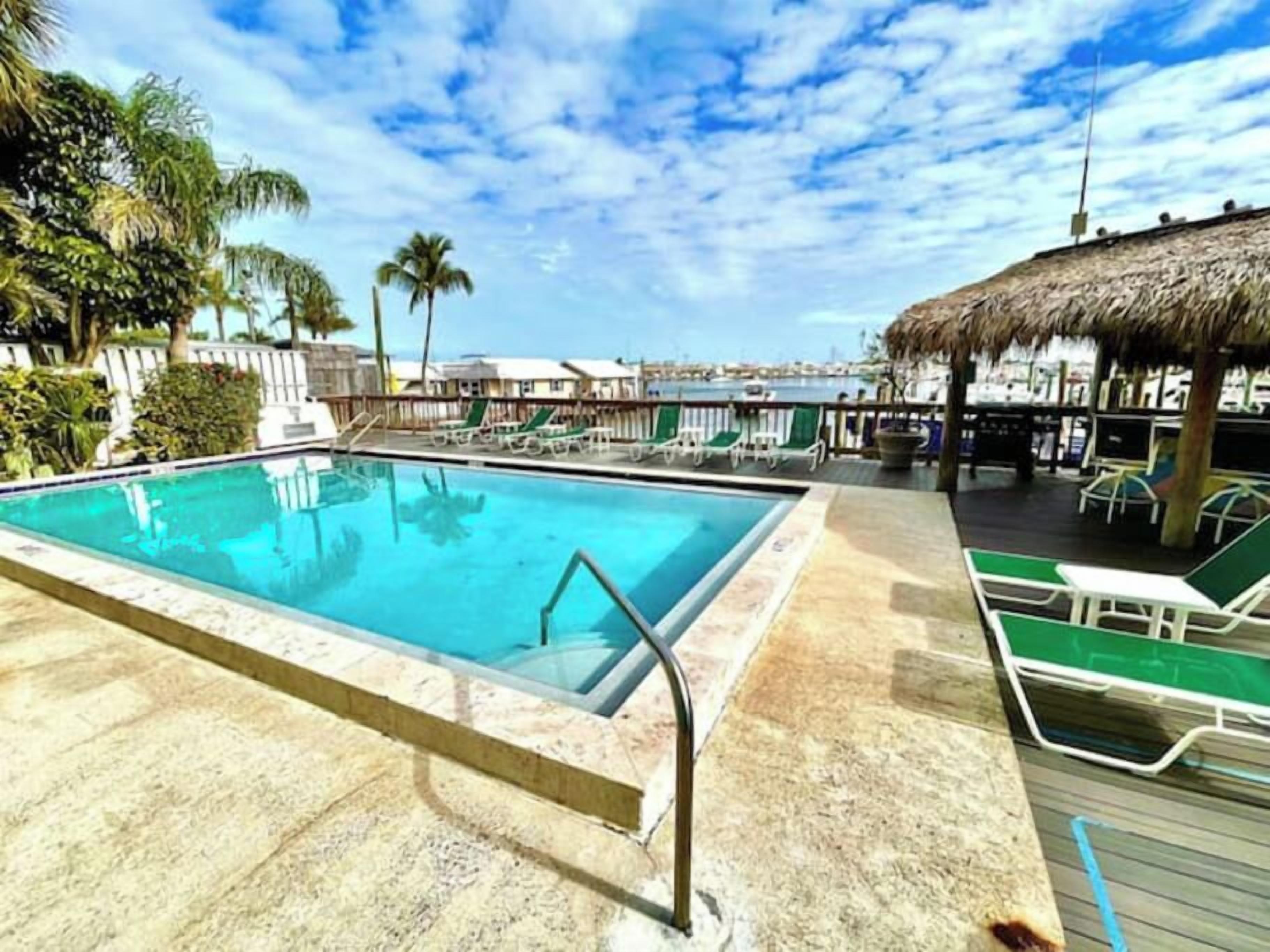 A swimming pool with a clear blue water, surrounded by lounge chairs and a thatched roof structure.