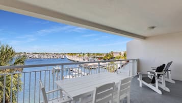 A balcony with a table and chairs, overlooking a marina with boats and a coastal town.