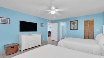 A bedroom with two beds, a television, and a ceiling fan.