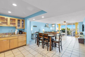 A modern kitchen with wooden cabinets, a dining area with a table and chairs, and a view of the ocean through large windows. - Waterfront Condo Dock Pool Near Duval St (Key West)