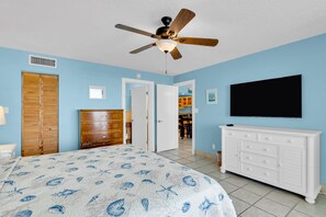 A bedroom with a bed, a dresser, a ceiling fan, a TV, and a door leading to a bathroom. - Waterfront Condo Dock Pool Near Duval St (Key West)