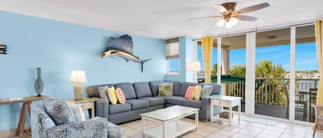 Un salon avec un mur bleu, un ventilateur de plafond, un canapé, une table basse et une vue sur l’extérieur.