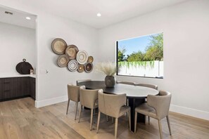 A modern dining area with a round table and six chairs, a vase with dried plants, and a wall-mounted plate collection. - Experience The Westly! Very Clean, Walk to Oldtown (Scottsdale)