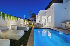 A modern outdoor pool area with a white wall, green plants, and a seating area with cushions. - Experience The Westly! Very Clean, Walk to Oldtown (Scottsdale)