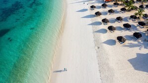 An aerial view of a beach with clear turquoise waters, white sand, and several thatched umbrellas. - Natural Kendwa Villa (Kendwa)