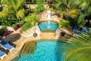 A pool surrounded by lush greenery and a waterfall, with lounge chairs and a stone pathway.