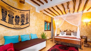 A room with a bed, a sofa, a red rug, and a wall with tribal art. - Natural Kendwa Villa (Kendwa)