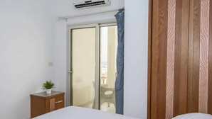 Een slaapkamer met een bed, een houten kledingkast, een klein kastje en een schuifdeur naar een balkon.