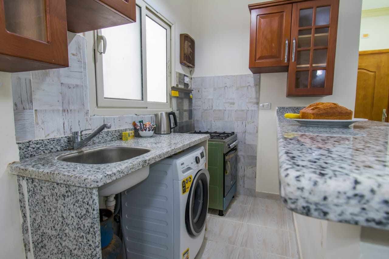Une cuisine dotée de plans de travail en granit, d’un lave-linge, d’une cuisinière et d’armoires en bois.