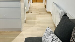 A narrow hallway with a wooden door at the end, a white cabinet with a cutting board on top, and a radiator on the right wall.