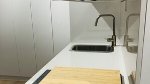 A modern kitchen with a white countertop, a wooden cutting board, and a stainless steel sink.