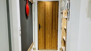 A hallway with a wooden door, a red object on a wall, and a shelf with items.