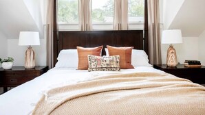 A neatly made bed with a dark headboard, two bedside tables with lamps, and a window with curtains.