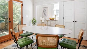 A dining area with a round table, green cushioned chairs, and a white cabinet in the background.