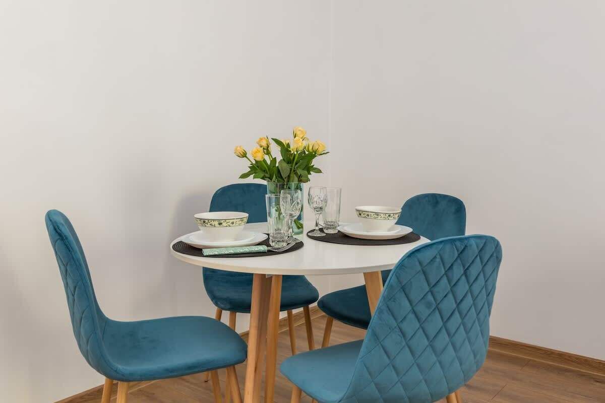 A dining table with four blue chairs, a vase with yellow flowers, and a set of plates and glasses.