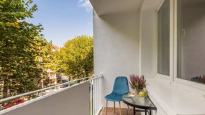 Un balcon avec une table et des chaises, une fenêtre et une vue sur les arbres et les bâtiments.
