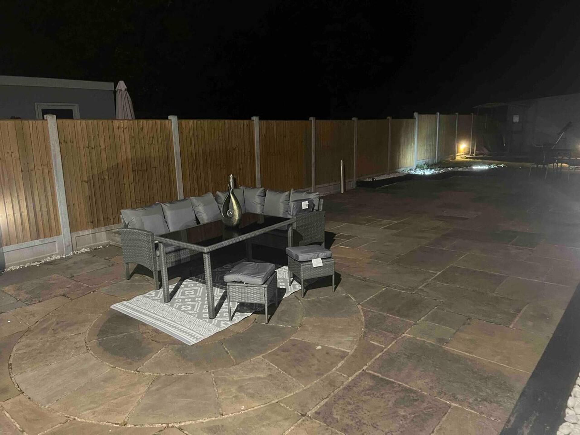 Un patio exterior con mesa de vidrio, asientos acolchados y alfombra estampada.