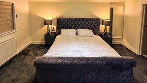 A bedroom with a large bed, a chandelier, and two bedside tables with lamps. - Serenity Haven 4-bed With Hottub,games,gym & More (Colchester)