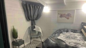 A modern bathroom with a bathtub, a shower, a chair, a small table with a plant, and a patterned rug. - Serenity Haven 4-bed With Hottub,games,gym & More (Colchester)