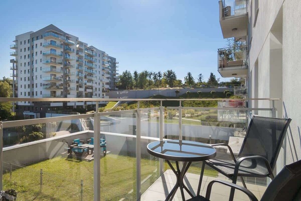 A balcony equipped with two chairs and a small table, overlooking a waterfront residential area.