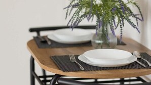 A dining table with two white plates, a glass vase with green foliage, and a fork and spoon on a black placemat. - Comfortable Studio in Praga | Parking and Air Conditioning (Warszawa)