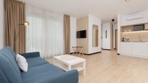 A modern living room with a blue sofa, a white coffee table, and a kitchen area with white cabinets and a microwave. - Comfortable Studio in Praga | Parking and Air Conditioning (Warszawa)