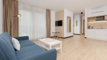 Una sala de estar moderna con un sofá azul, una mesa de centro blanca y una cocina con armarios blancos y un microondas.