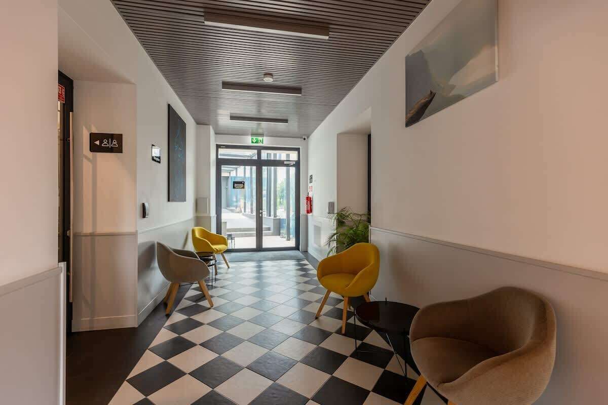 Una hall d'albergo con pavimento a scacchi, sedie moderne e una porta che dà all'ingresso.