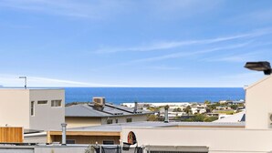 A coastal residential area with modern buildings, a clear sky, and a view of the ocean. - Newly Built 3 Bedroom Townhouse with Ocean Views (Torquay)