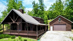 A rustic cabin with a porch, a garage, and a gravel driveway.