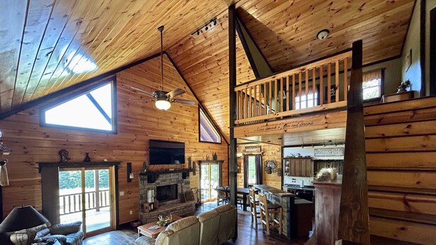 A spacious log cabin interior with a living room, sofa, fireplace, kitchen, and a balcony.