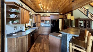 A kitchen with wooden cabinets, granite countertops, a central island, and a staircase leading to another level.