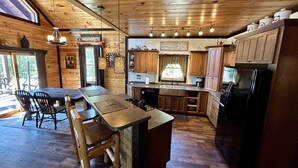 A rustic kitchen with wooden cabinets, a black refrigerator, and a dining area with wooden chairs and a table.