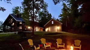A cabin with a porch and a fire pit area with chairs.