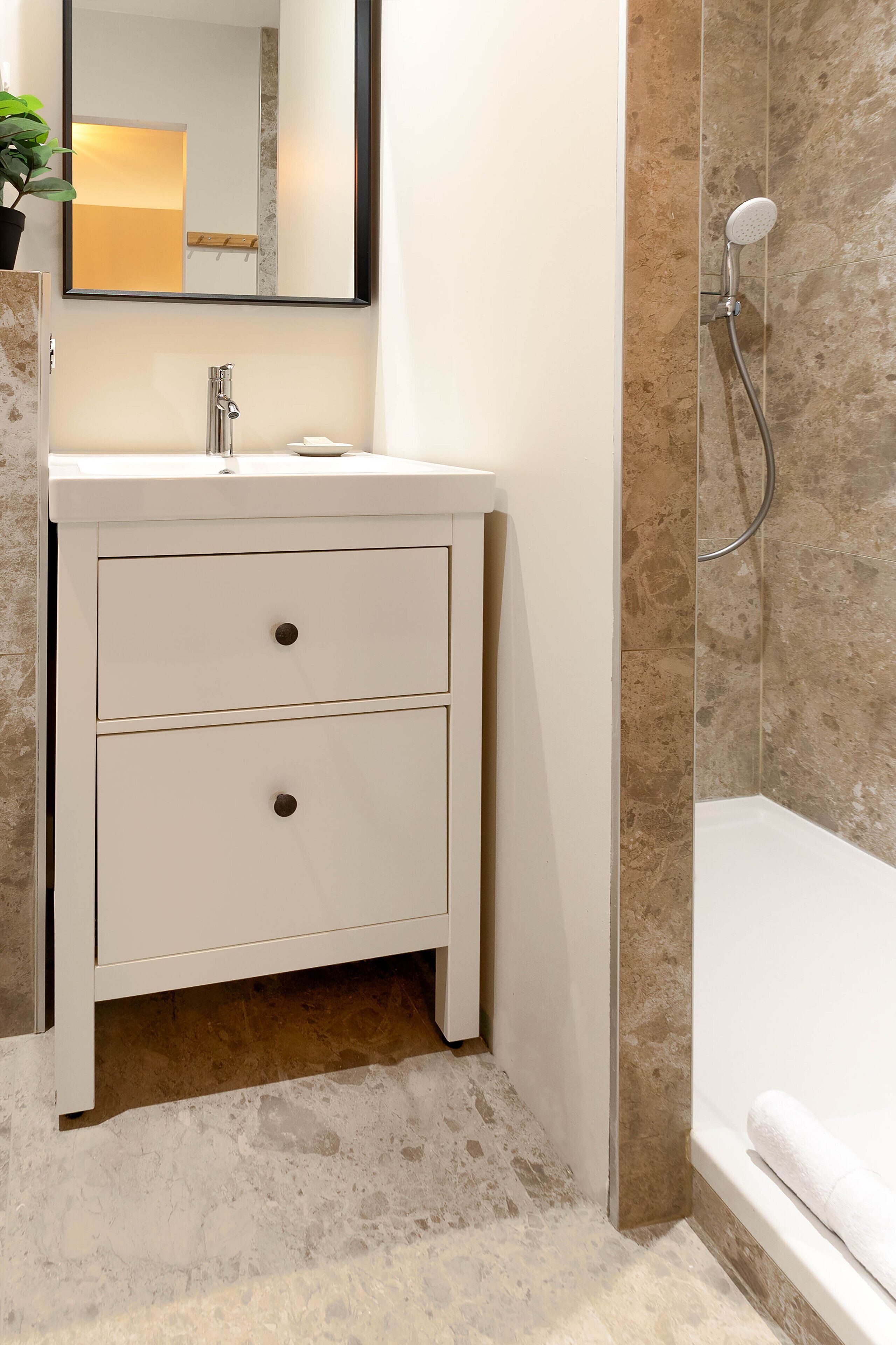 A bathroom with a white vanity, a mirror, a shower, and a towel on the floor.