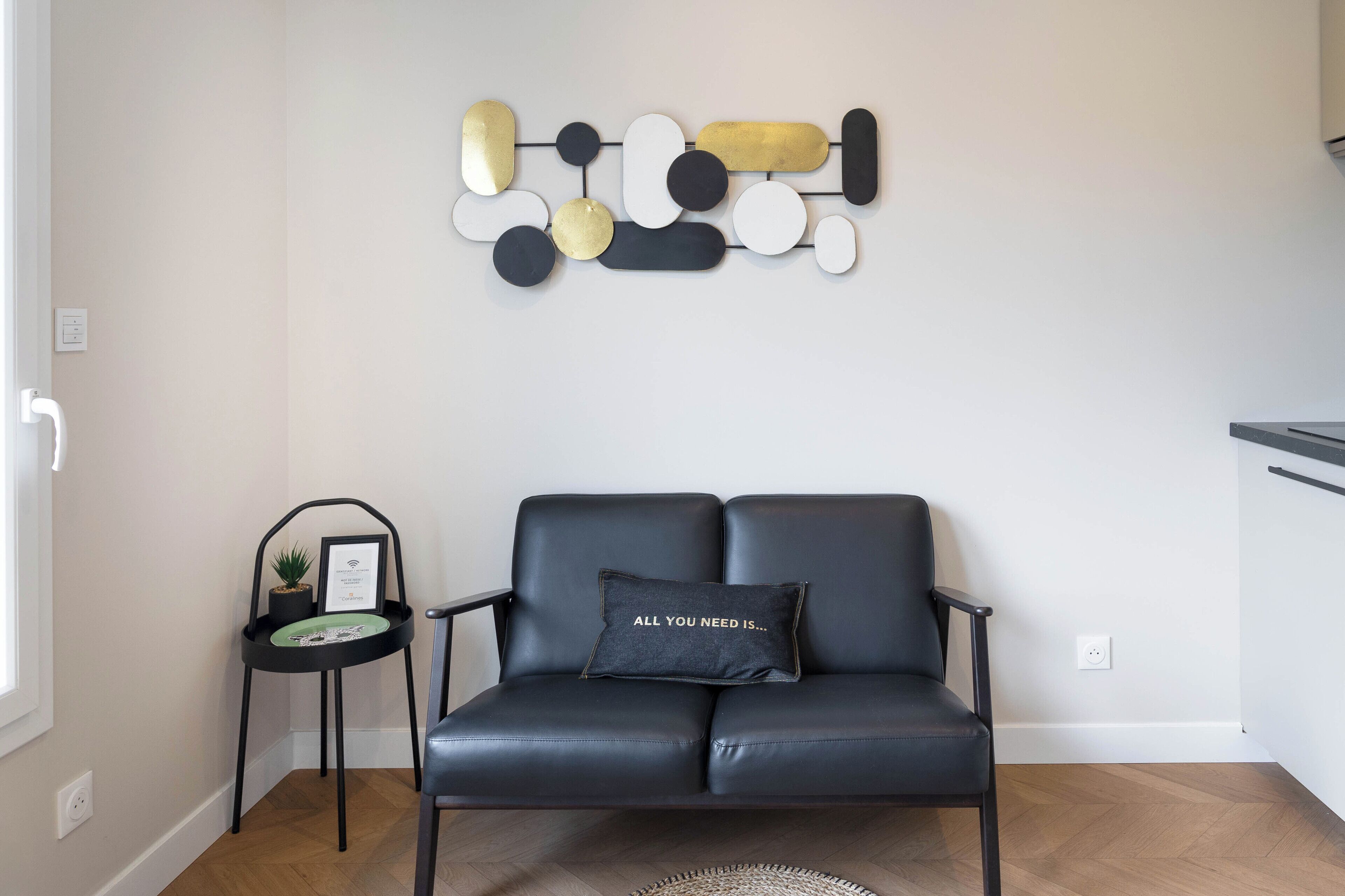 A modern living room with a black leather sofa, a small side table with a plant, and a wall art piece.