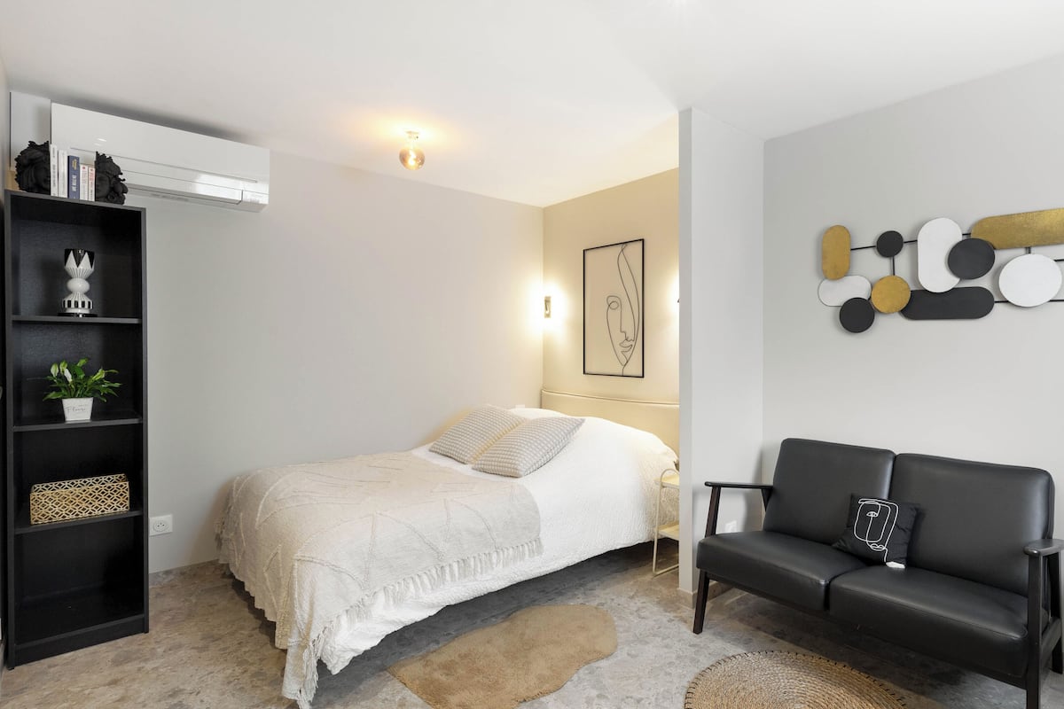 Quarto moderno com cama, sofá preto, obra de arte na parede e estante.
