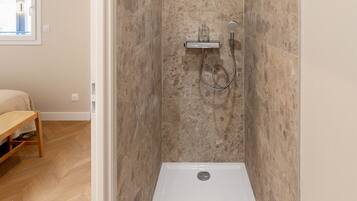 A small, modern bathroom with a shower, a wooden bench, and a window.