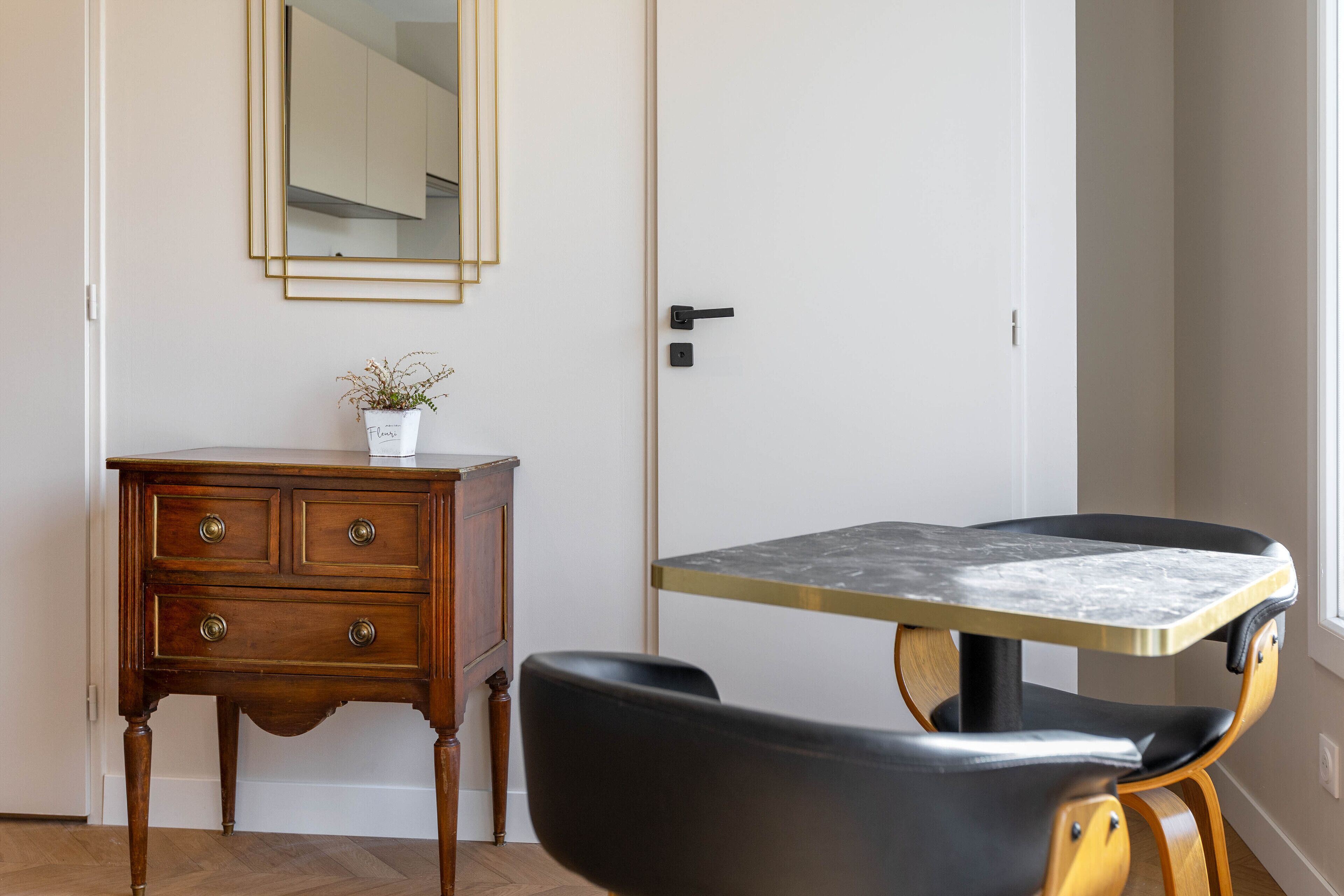 A room with a wooden dresser, a small potted plant, a black chair, and a table with a marble top.