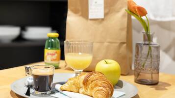 A breakfast tray with a croissant, coffee, juice, and an apple on a wooden table.