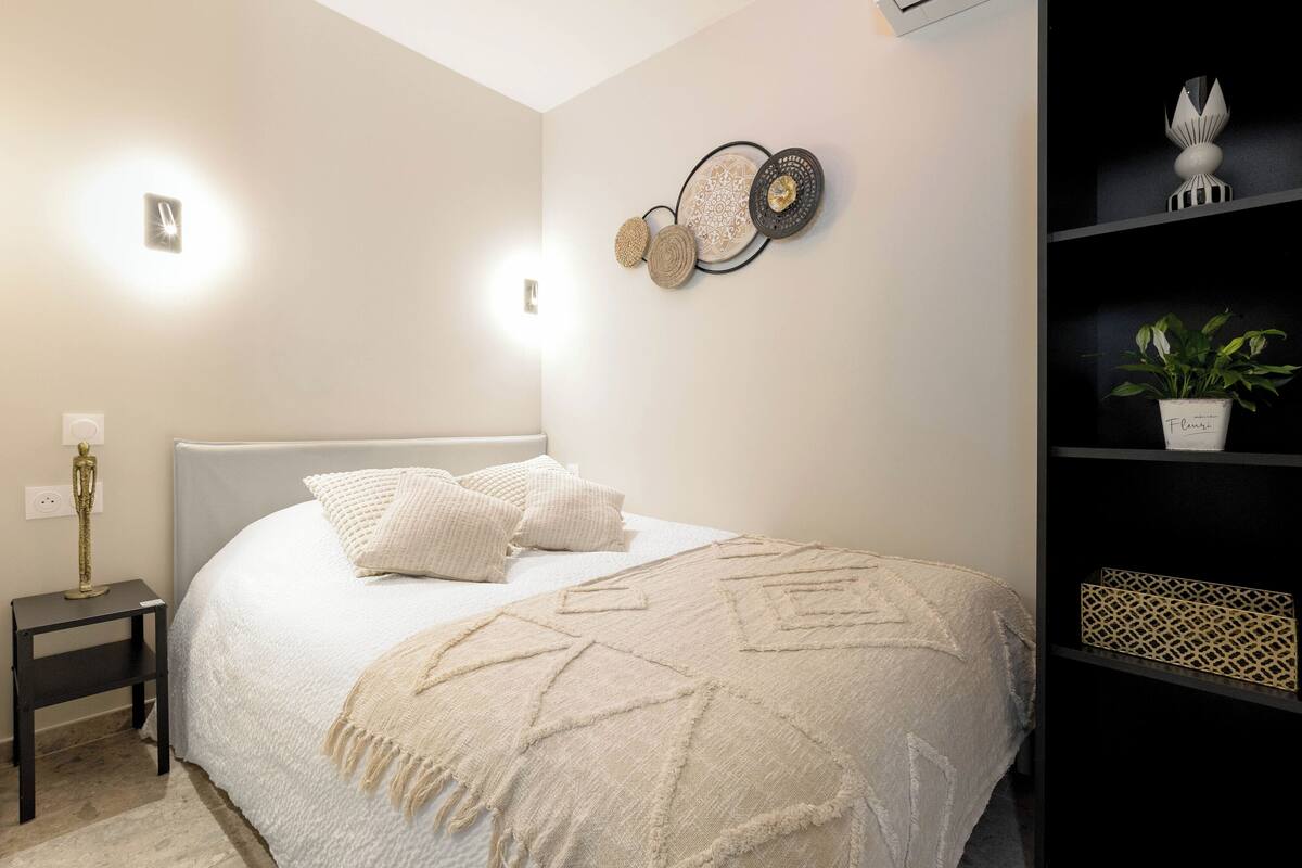 Quarto com cama, mesa de cabeceira, decoração na parede e um prateleira com uma planta.