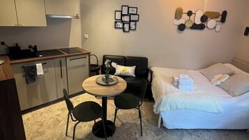 Ein kompakter Wohnbereich mit Küchenzeile, Essplatz, Sofa und Bett.