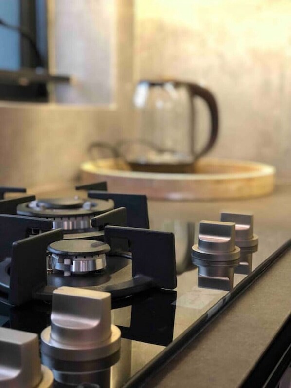 A kitchen with a gas stove, a coffee maker, and a kettle on the counter.