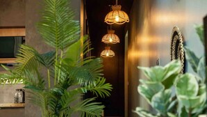 Un pasillo con lámparas colgantes, un estante de madera con un recipiente de vidrio y plantas verdes.