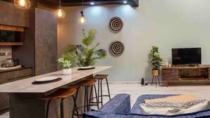 Una cocina moderna con una isla central, iluminación colgante y un televisor de pantalla plana sobre un soporte de madera.