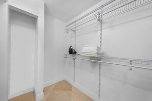 Um closet amplo com prateleiras metálicas, uma porta branca e piso bege.