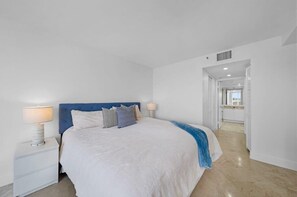 A modern bedroom with a large bed, white nightstands, and a blue headboard.