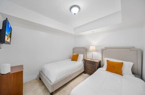 A hotel room with two beds, a nightstand, a lamp, a TV, and a wooden dresser.