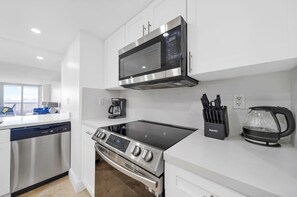 A modern kitchen with white cabinets, a stainless steel dishwasher, a built-in oven, a microwave, and a coffee maker.
